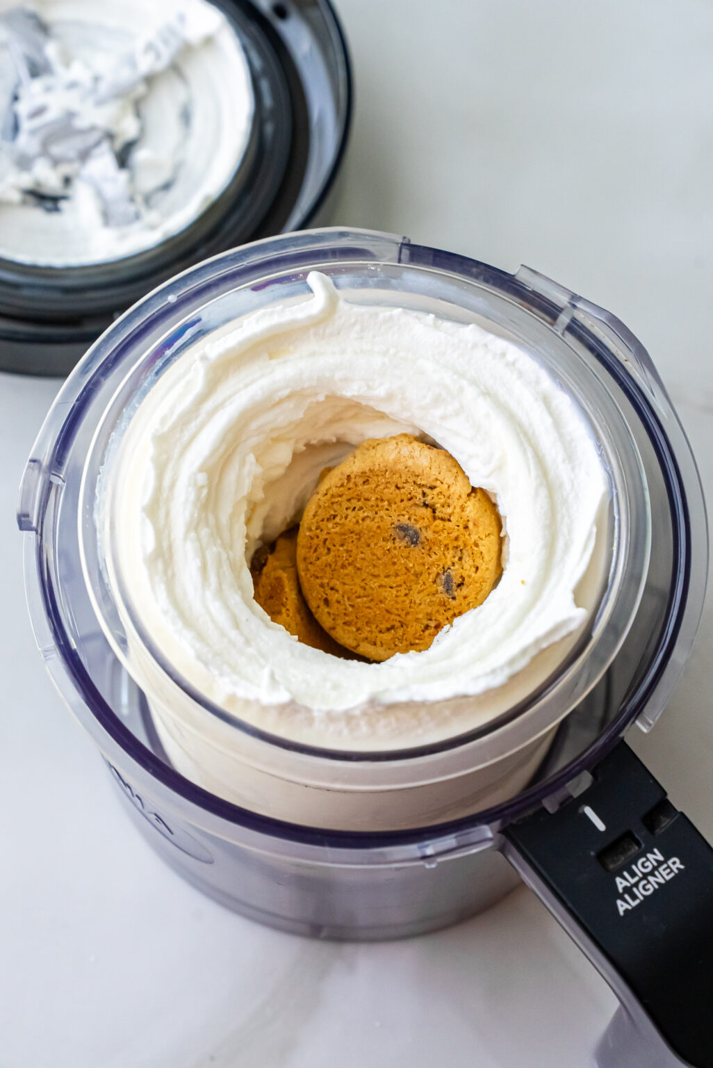 Top-down view of whole Girl Scout Caramel Chocolate Chip cookies placed into the center well of spun white ice cream in a Ninja Creami pint, ready for final “Mix-In” cycle to create High Protein Caramel Chocolate Chip Ninja Creami Ice Cream.