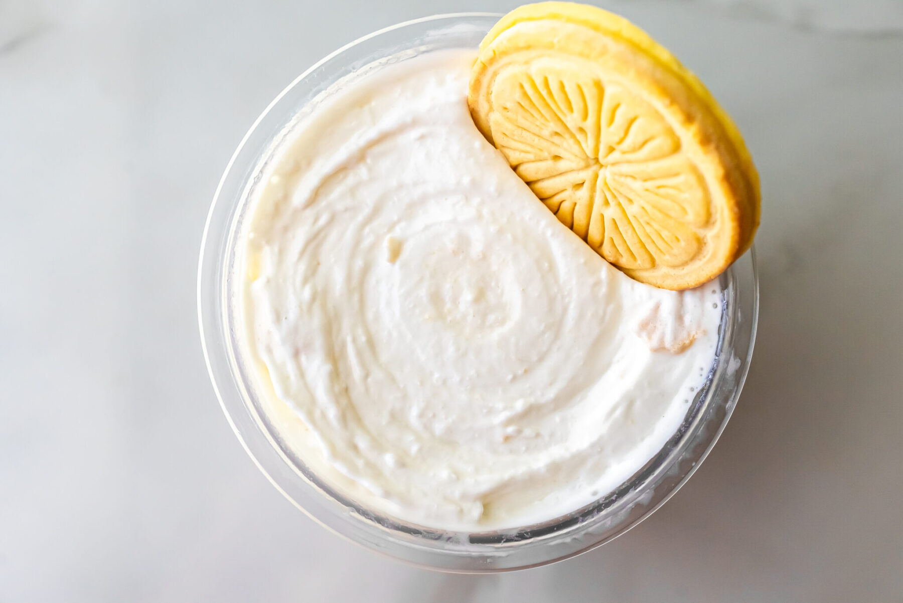 Overhead shot of creamy white Lemonades Ninja Creami Ice Cream in a pint. A yellow Lemonades cookie is placed on the right side of the surface, contrasting with the smooth white base.