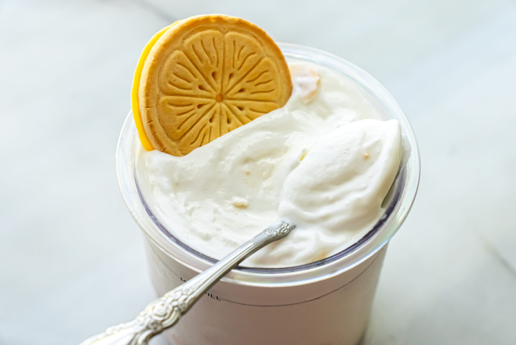 Side view of Lemonades Ninja Creami Ice Cream in a pint. A Lemonades cookie garnishes the top while a decorative silver spoon is inserted into the creamy mixture.