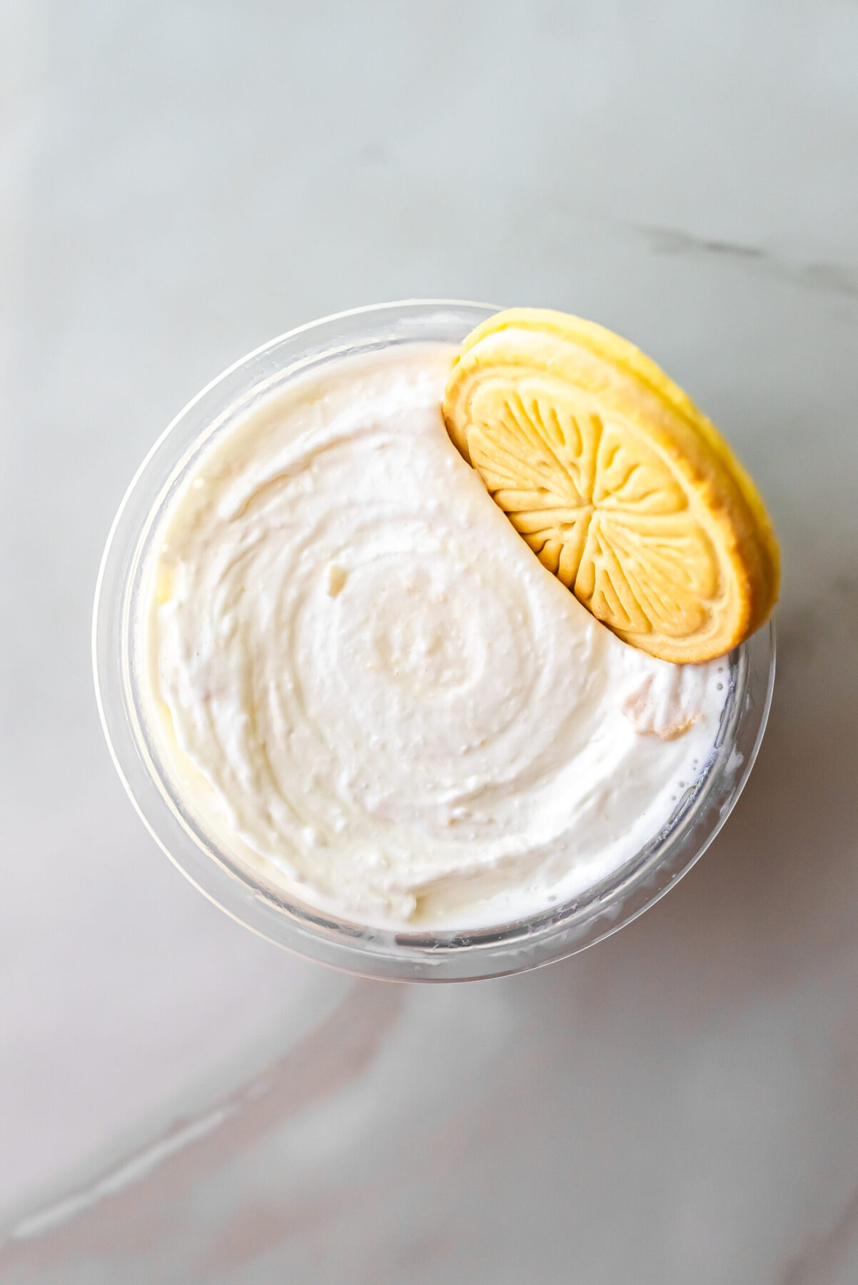 Overhead shot of smooth white Lemonades Ninja Creami Ice Cream in a pint. A yellow Girl Scout Lemonades cookie rests on the upper right edge of the creamy surface.