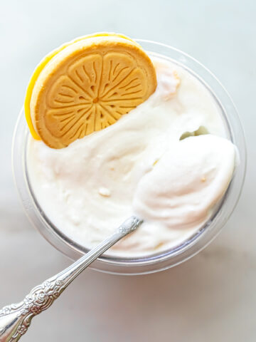 Overhead view of Lemonades Ninja Creami Ice Cream in a pint. An ornate silver spoon rests in the white ice cream, and a whole Lemonades cookie sits on the upper left edge of the container.Overhead view of Lemonades Ninja Creami Ice Cream in a pint. An ornate silver spoon rests in the white ice cream, and a whole Lemonades cookie sits on the upper left edge of the container.