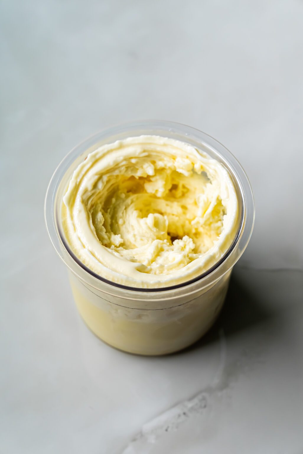 A clear plastic container filled with whipped butter sits on a light gray surface, reminiscent of the presentation style seen with low-carb Banana Protein Ice Cream freshly churned from a Ninja Creami.