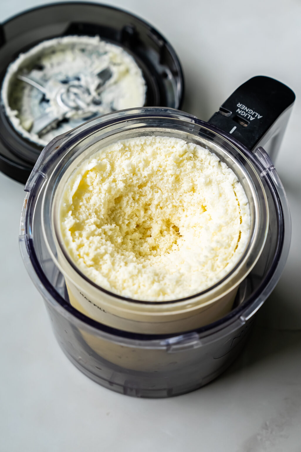 An open Ninja Creami filled with freshly grated cheese shows the cheesy goodness inside, with the metal blade covered in cheese residue on the lid.
