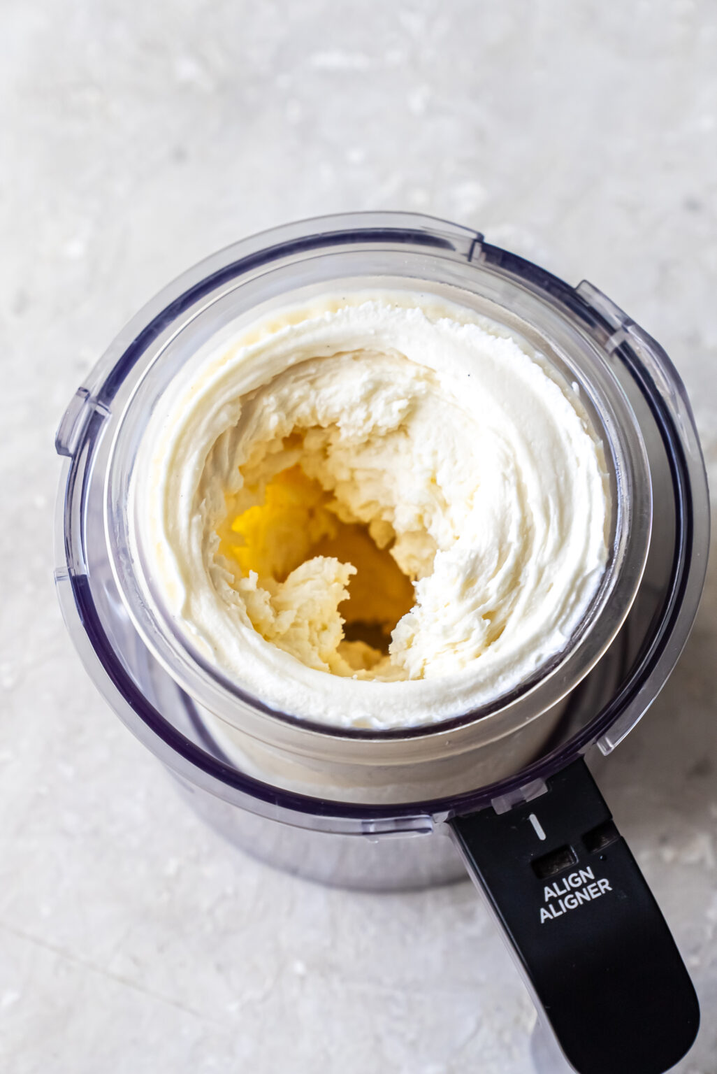 Top-down view of churned white ice cream in a Ninja Creami pint showing a hollow center well after the initial spin cycle for Mint Chocolate Protein Ice Cream.