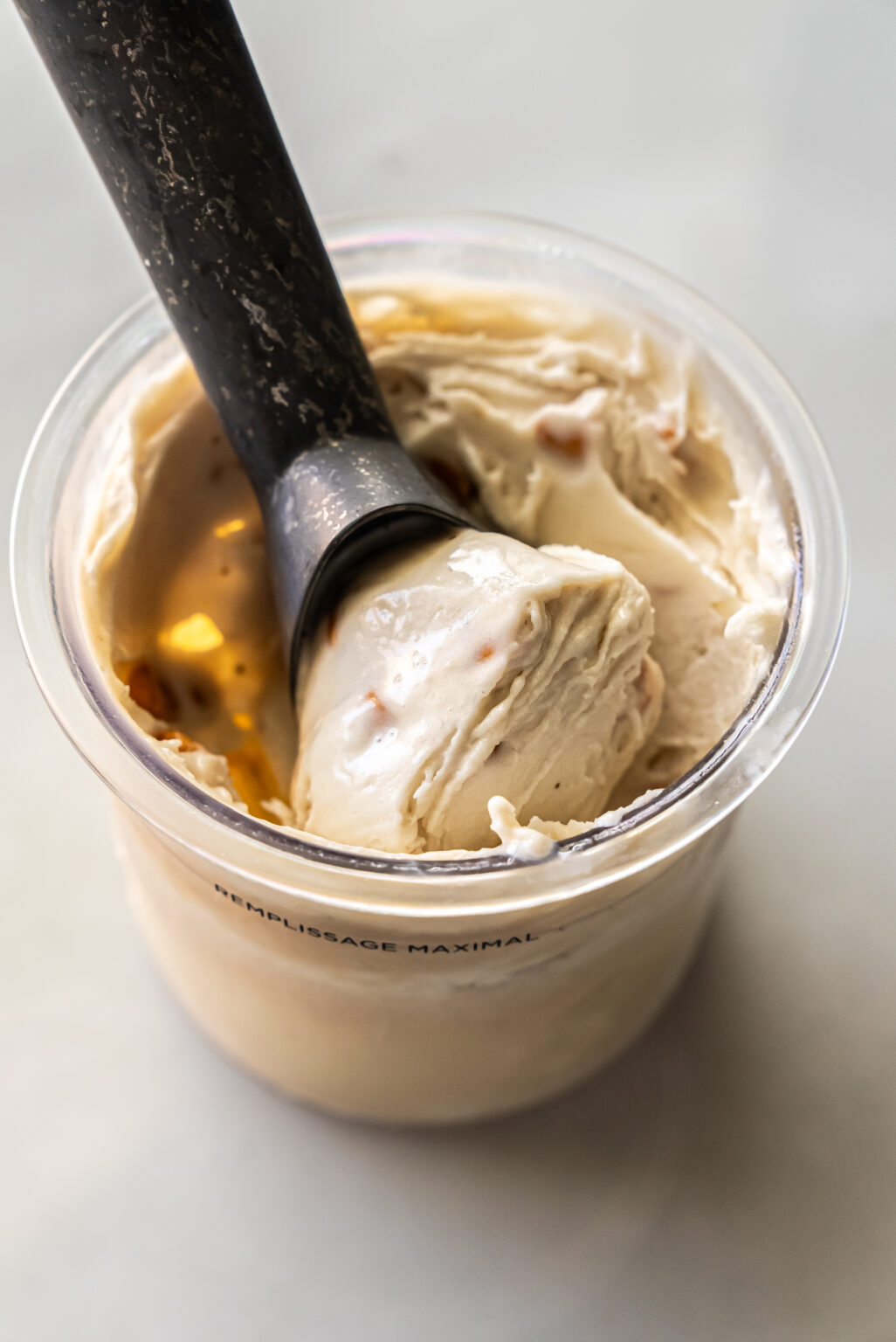 Close-up of creamy Ninja Creami Banana Ice Cream with protein powder in a clear pint, featuring visible butterscotch chips and a black spoon lifting a rich swirl, showcasing its thick texture.