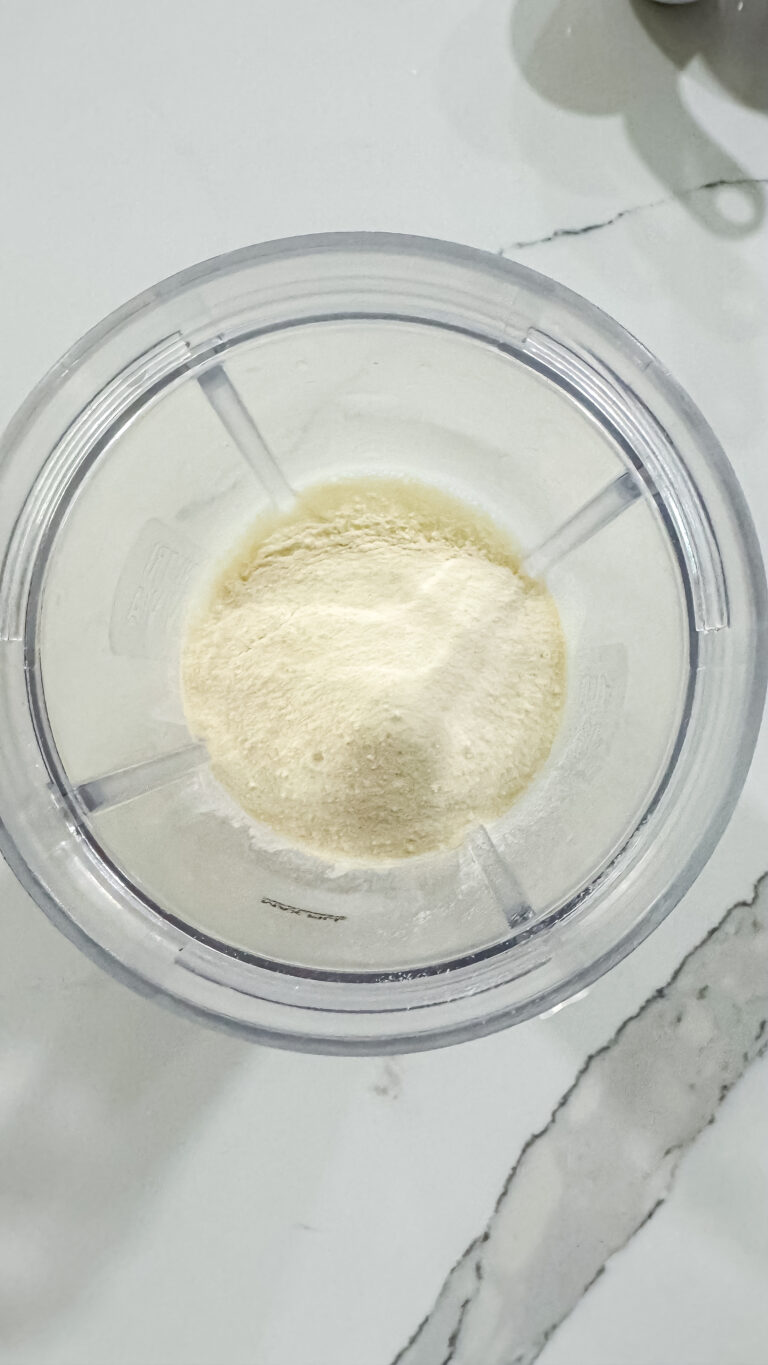 Top-down view of a clear Ninja Creami pint containing light yellow protein powder mixed with liquid base, ready for blending to make Ninja Creami Banana Ice Cream with protein powder.