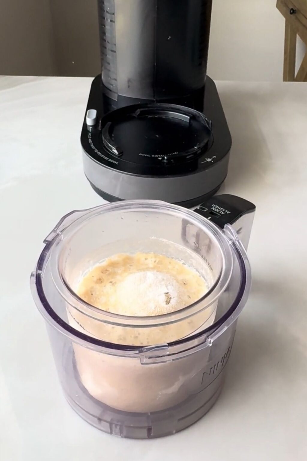 A Ninja Professional blender cup attached to its base, blending a creamy white liquid mixture to create the smooth base for Ninja Creami Banana Ice Cream with protein powder.