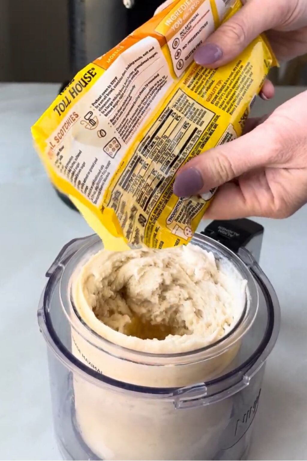 Hands pouring Toll House butterscotch chips into a Ninja Creami pint filled with churned banana ice cream base, adding mix-ins for Ninja Creami Banana Ice Cream with protein powder.