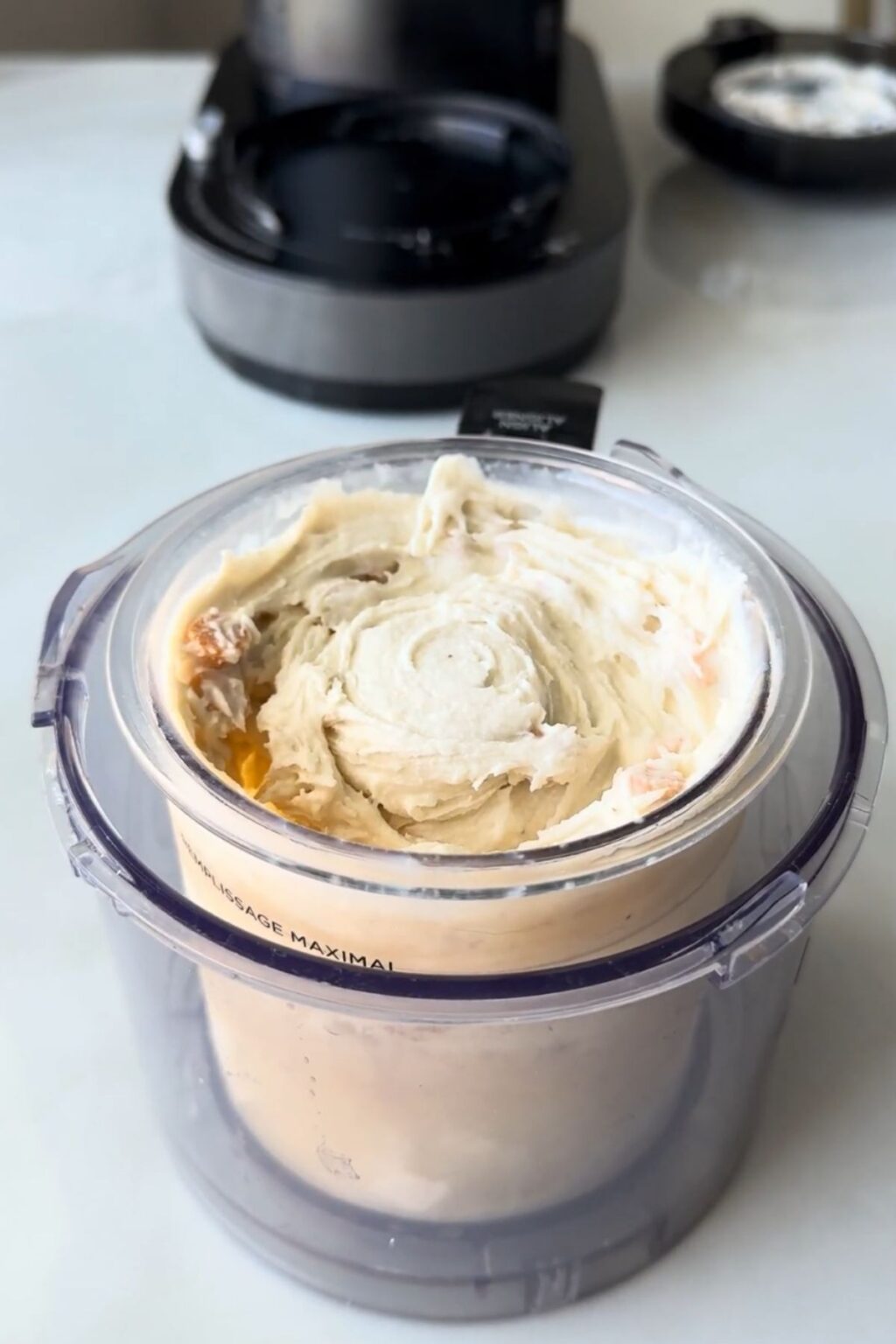 A Ninja Creami clear pint attached to its base, with a recently churned creamy white ice cream made in Ninja Creami.