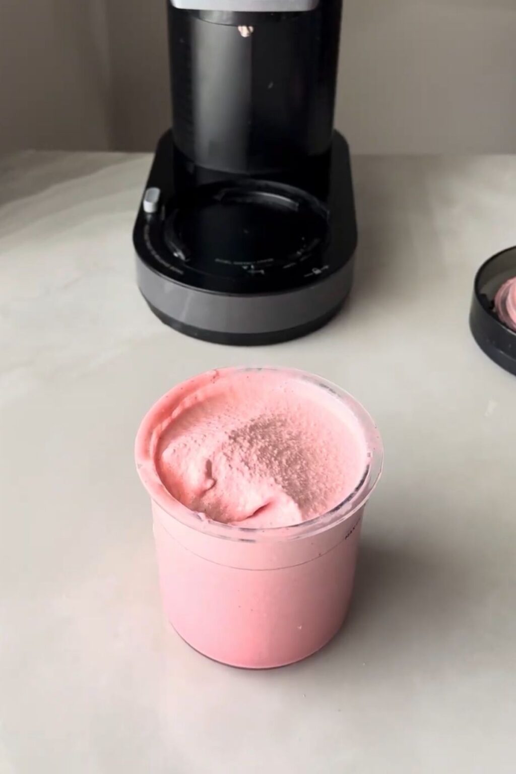 Top-down view of a clear Ninja Creami pint filled with vibrant pink cherry protein ice cream, showing a smooth, slightly textured surface after churning, ready to be served or mixed with toppings.