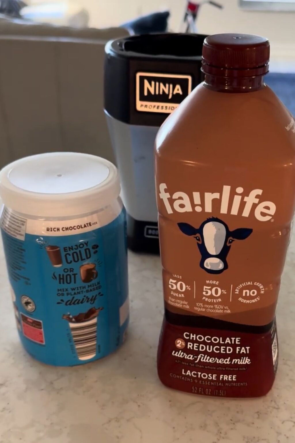 Fairlife chocolate milk and a tub of rich chocolate malt powder sit beside a Ninja Professional blender, showcasing key ingredients for making Ninja Creami Chocolate Malt Ice Cream at home.