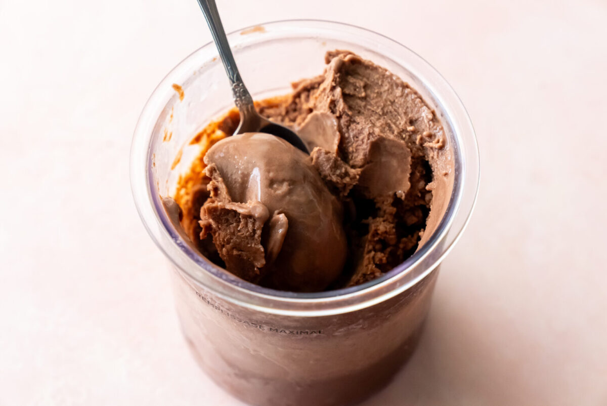 Close-up of a silver spoon digging into a pint of Ninja Creami Chocolate Malt Ice Cream, revealing its thick, velvety consistency and deep brown color, ready to be enjoyed straight from the container.