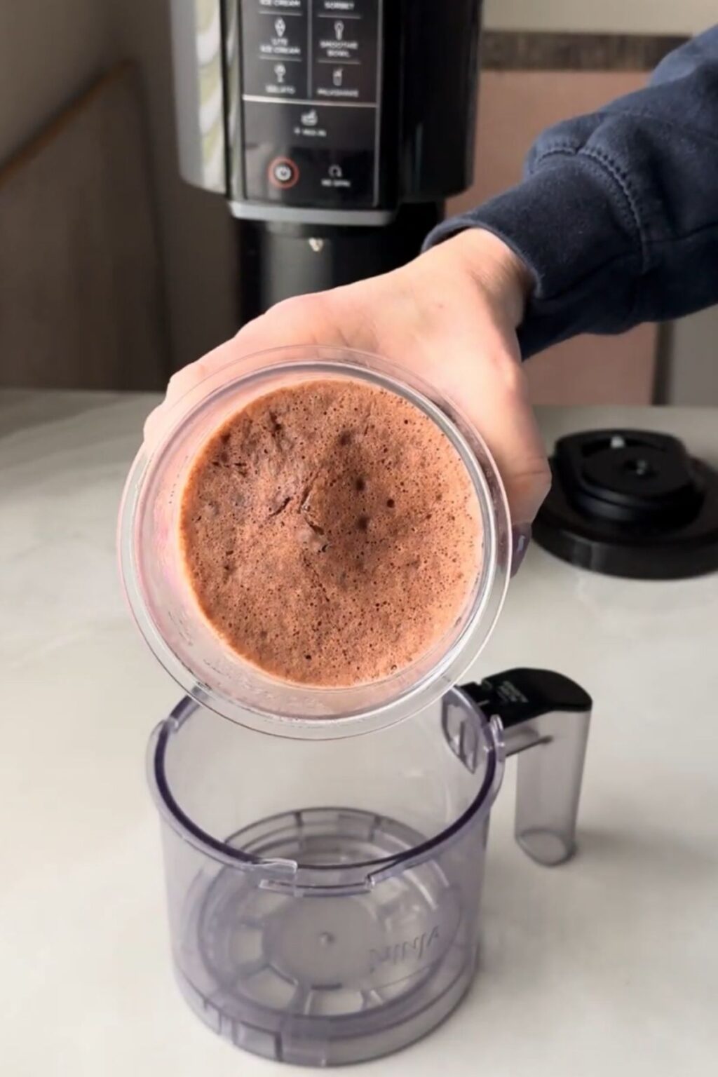 A top view of a hand holding a pint of frozen light brown chocolate malt mixture.