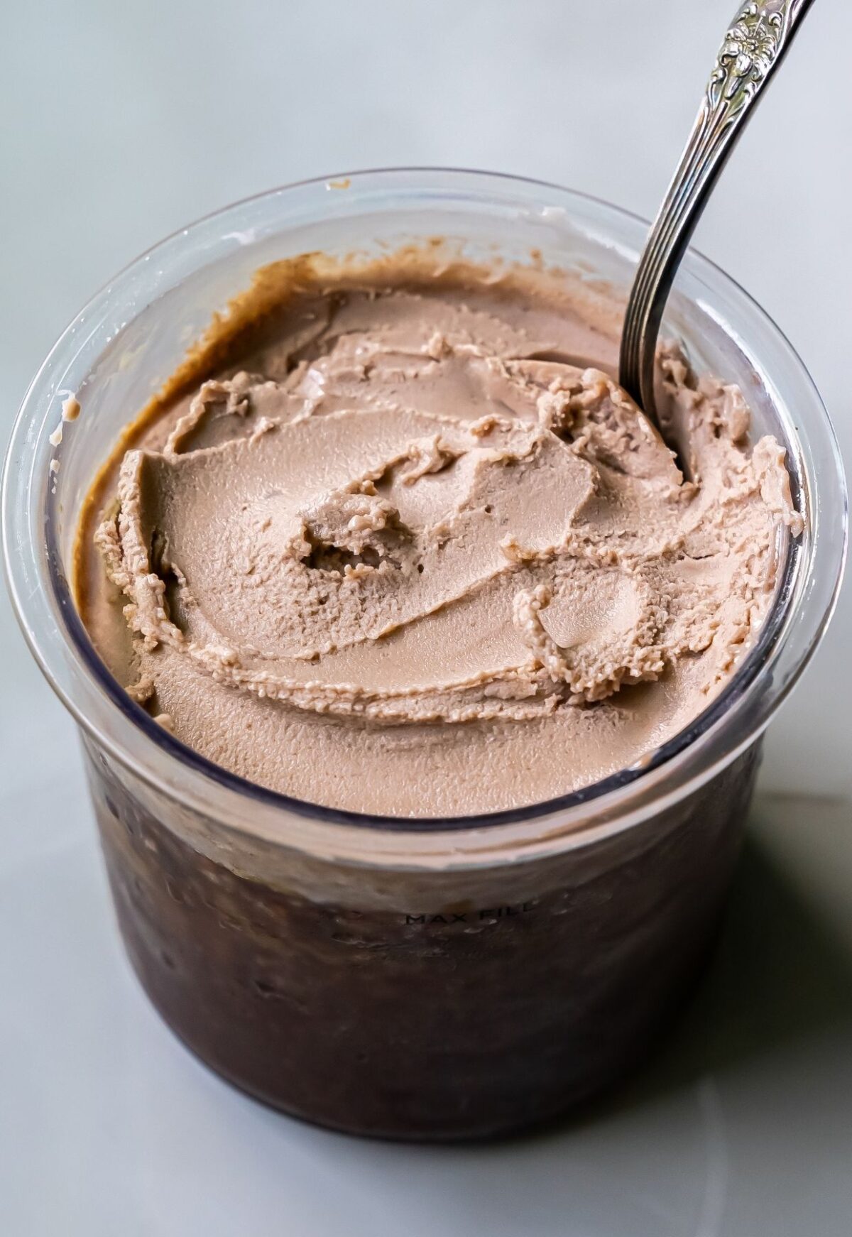 A container filled with light brown, dairy-free ice cream, partially scooped with a spoon—crafted to perfection using the Ninja Creami.