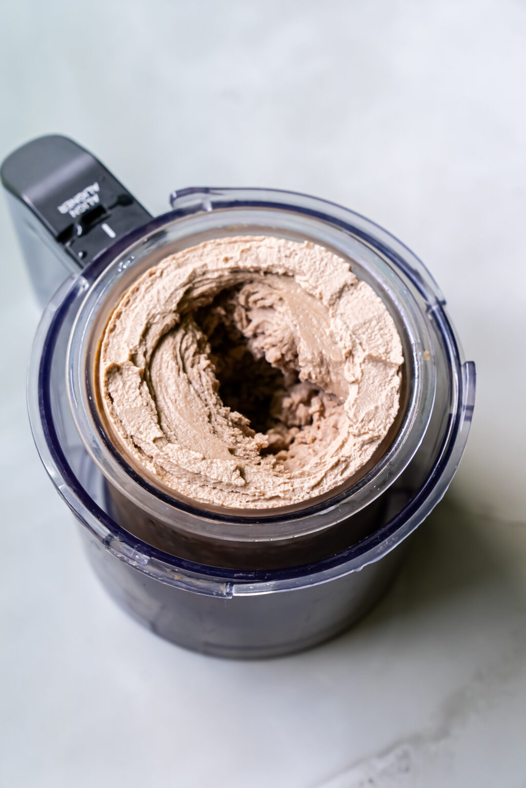 Top view of dairy-free chocolate peanut butter ice cream being churned in an ice cream maker against a light-colored background.