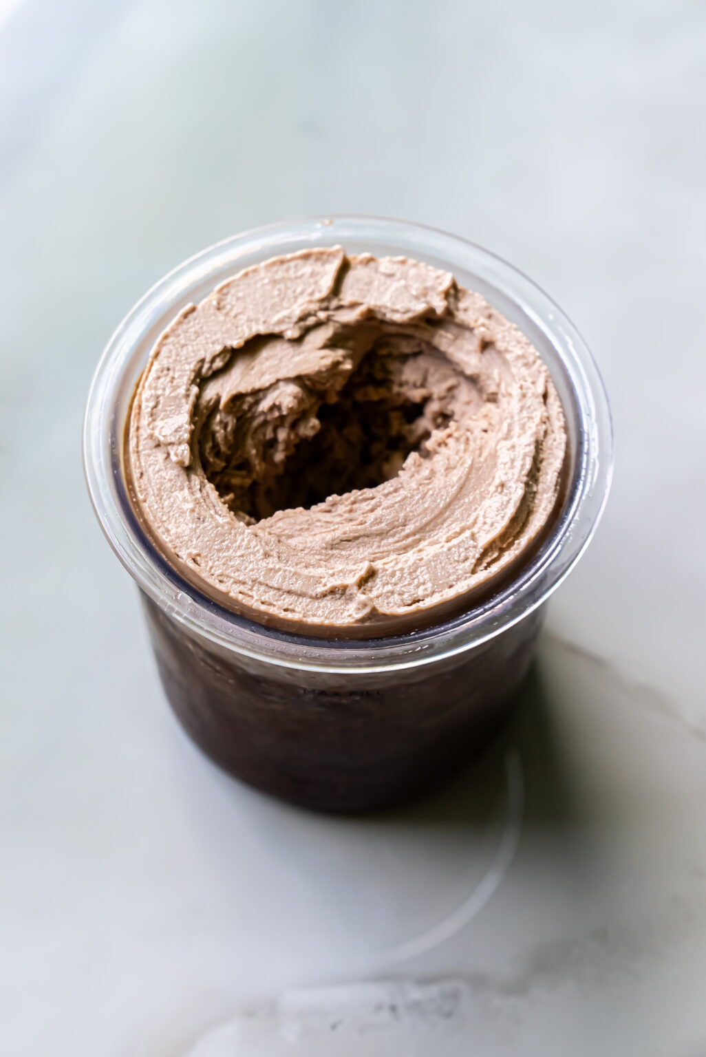 A clear plastic container filled with creamy, dairy-free, chocolate-flavored mousse with a smooth swirl pattern on top.