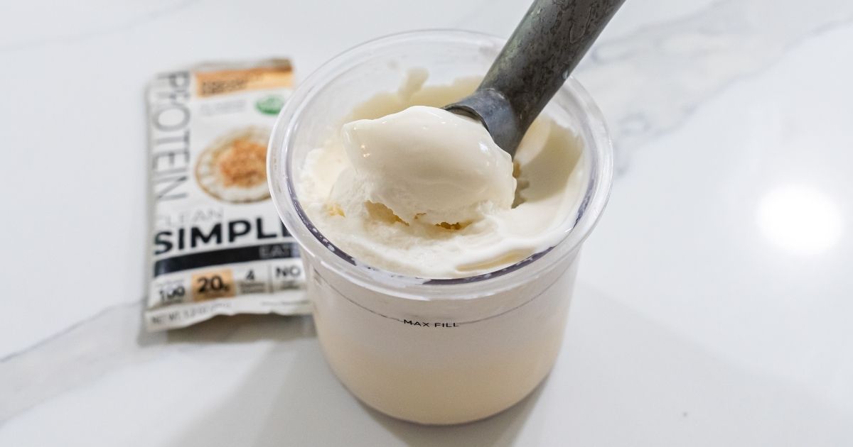 A spoon rests in a container of coconut with a protein powder sachet beside it on a white surface, ready to be transformed into a delicious Protein Ice Cream using the Ninja Creami.