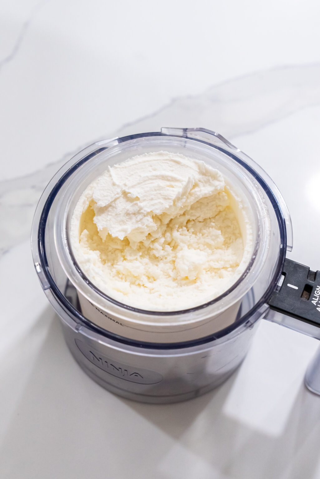 A food processor filled with a thick, creamy Keto mixture sits on a white countertop.
