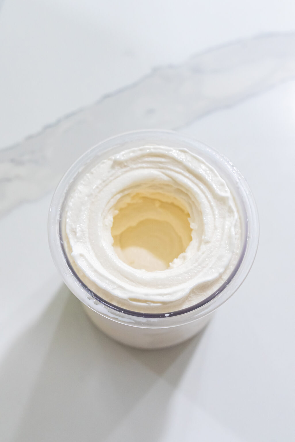 A top view of a Keto-friendly container filled with white, fluffy whipped cream on a light-colored surface, perfect for use with the Ninja Creami.