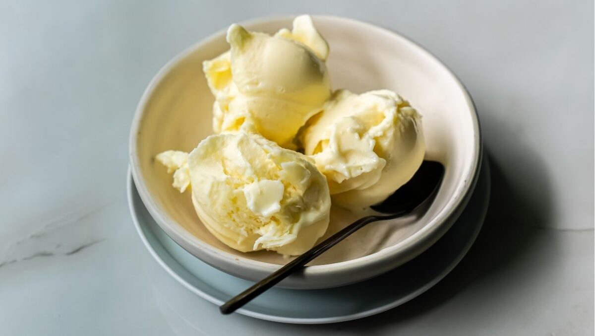 Three scoops of vanilla protein ice cream in a white bowl, with a metal spoon on the side.