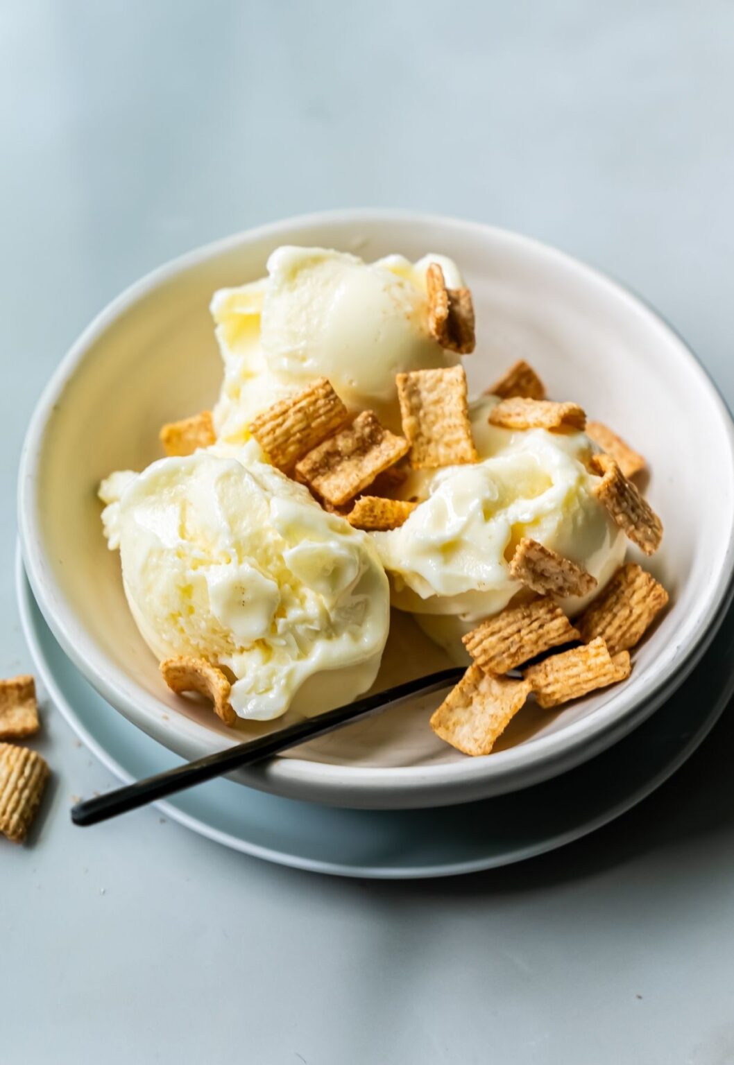 A bowl of vanilla ice cream, freshly churned using a Ninja Creami, topped with breakfast cereal squares on a white dish with a silver spoon on the side.