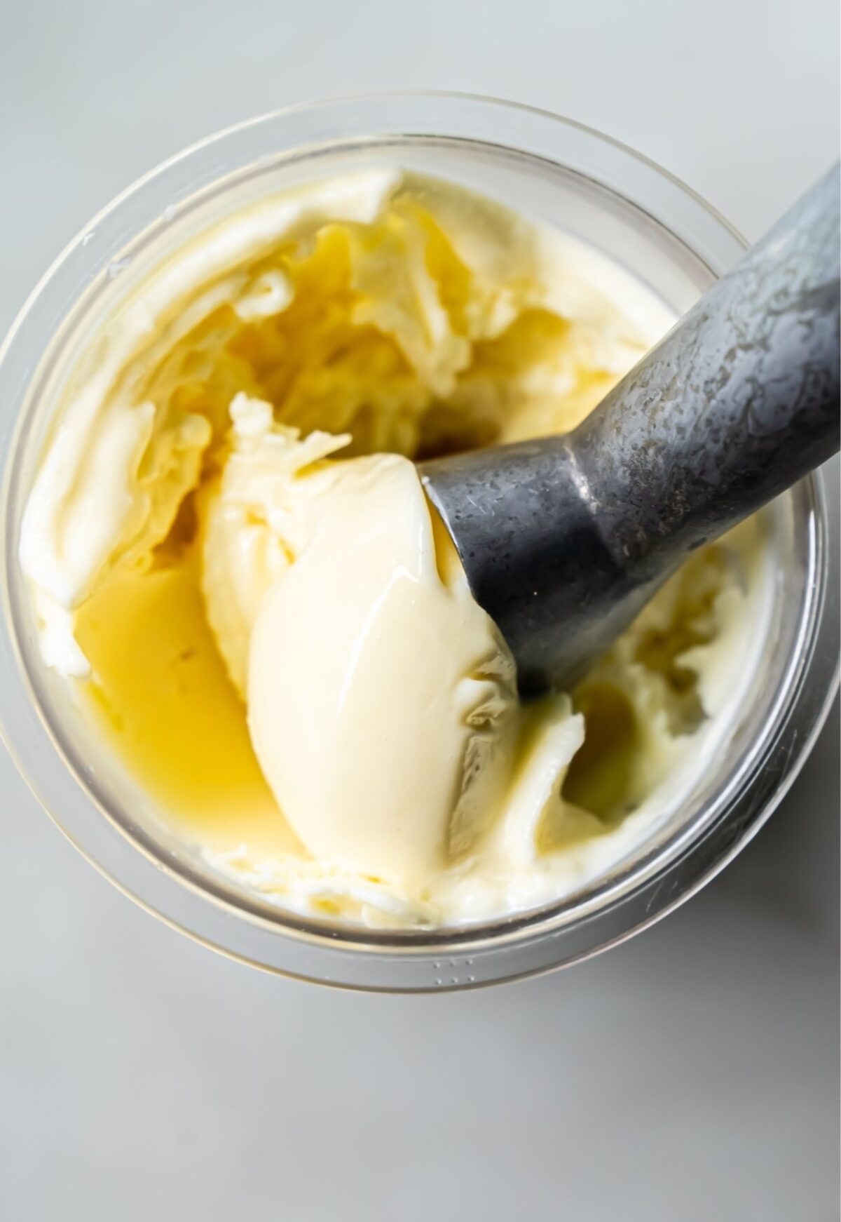 A metal scoop is shown in a container of pale yellow, low-carb ice cream made with the Ninja Creami, capturing a smooth and creamy texture.