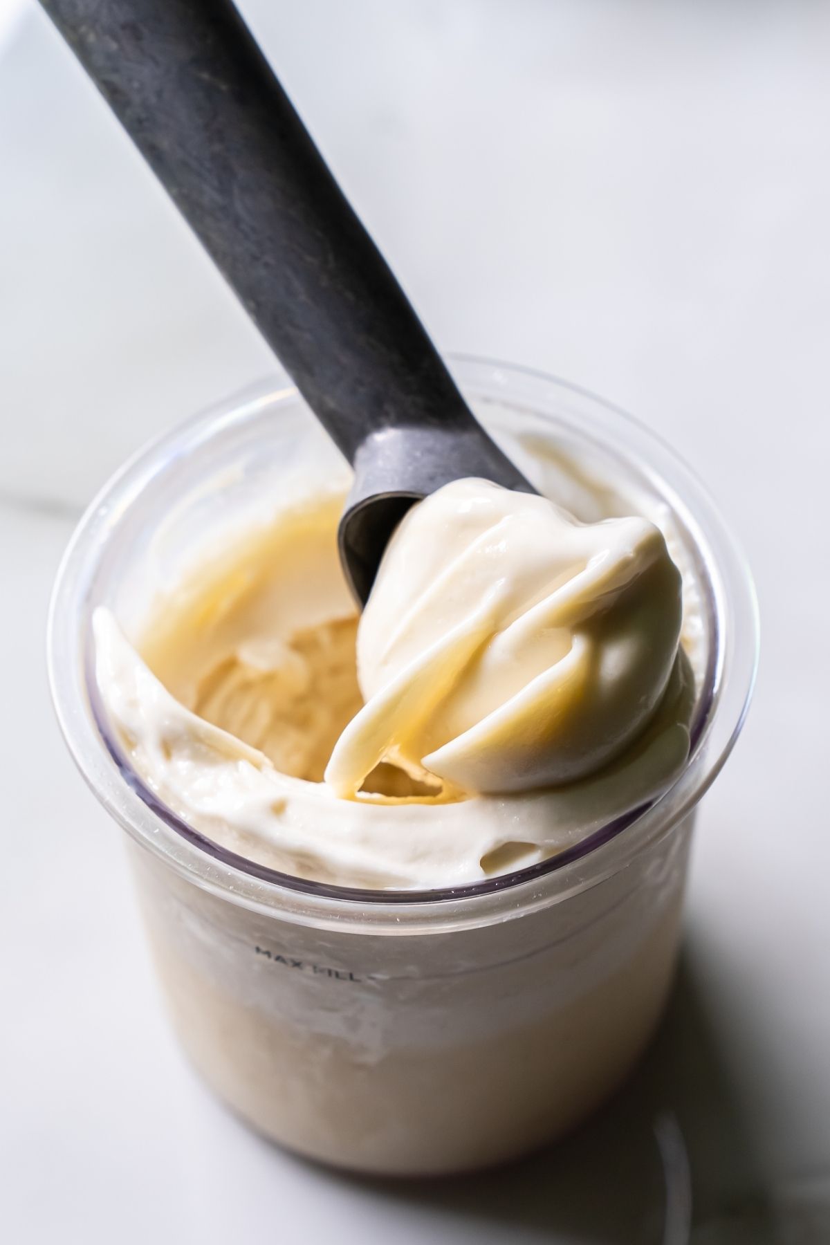 Close-up of creamy white Ninja Creami Oat Milk Coconut Protein Ice Cream in a clear pint, with a black spoon lifting a smooth swirl, showcasing its rich texture and consistency.