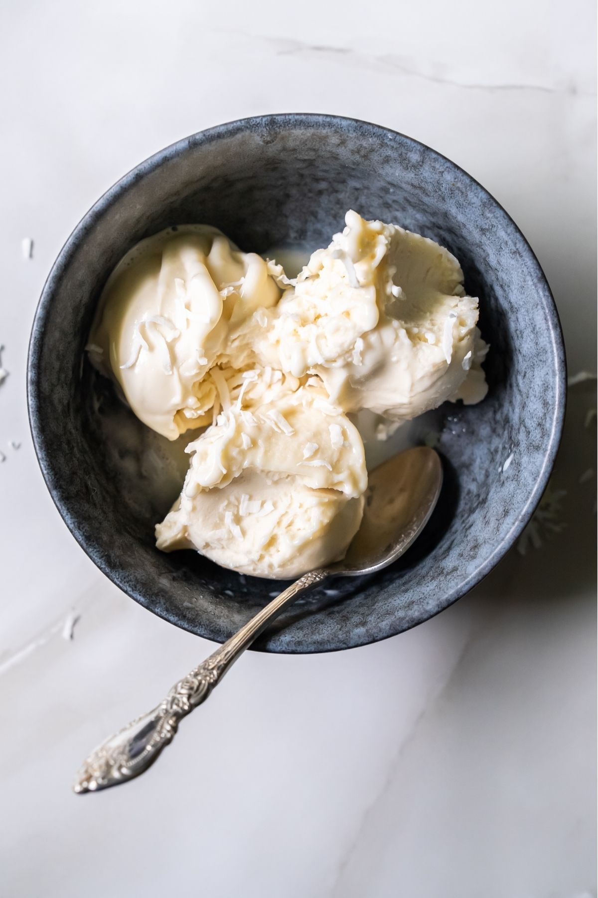 A black bowl filled with three scoops of creamy ice cream, made using the Ninja Creami, with a metal spoon resting inside the bowl.