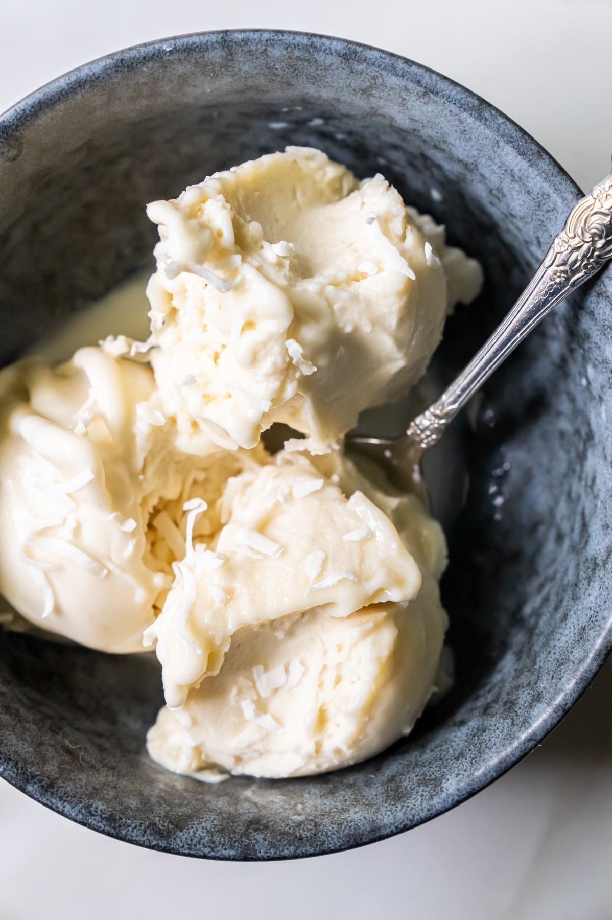 A black bowl filled with three scoops of creamy ice cream, made using the Ninja Creami, with a metal spoon resting inside the bowl.
