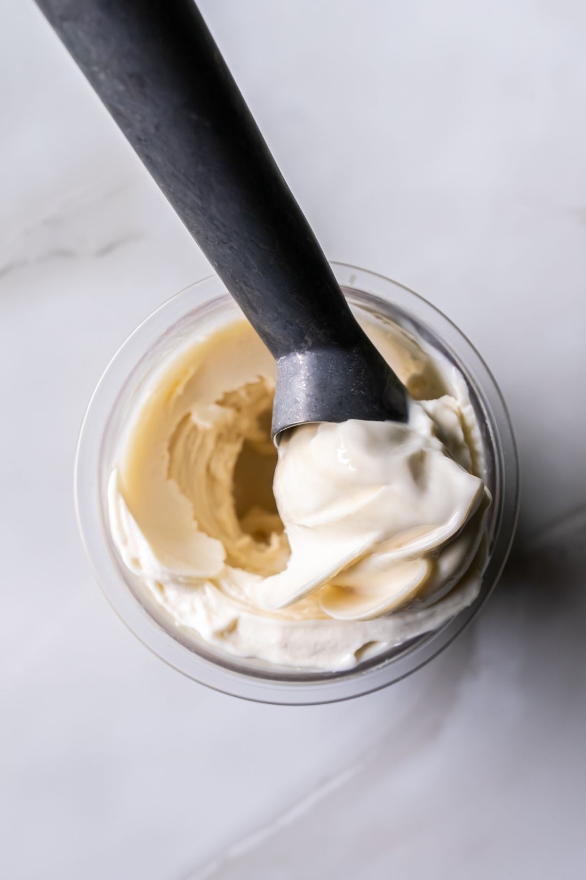 Top view of creamy white Ninja Creami Oat Milk Coconut Protein Ice Cream in a clear pint, with a black spoon lifting a smooth swirl, showcasing its rich texture and consistency.