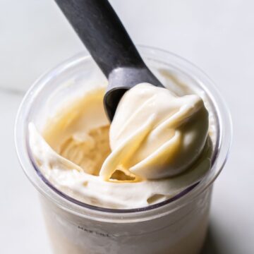 Close-up of creamy white Ninja Creami Oat Milk Coconut Protein Ice Cream in a clear pint, with a black spoon lifting a smooth swirl, showcasing its rich texture and consistency.