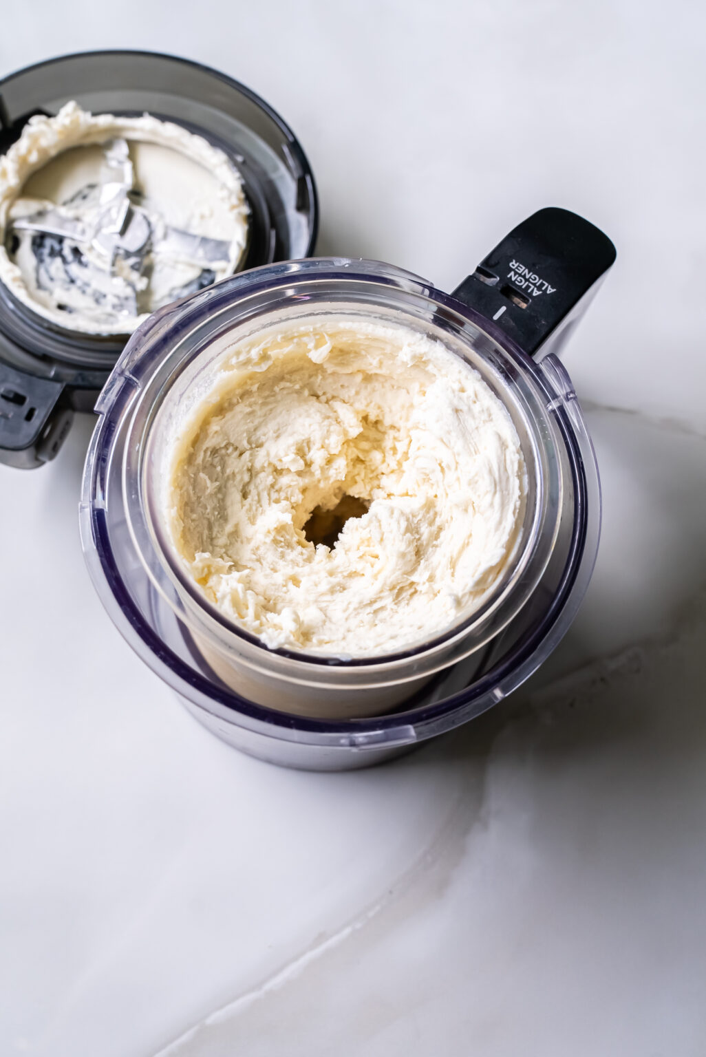An electric Ninja Creami ice cream maker sits on a white countertop, its transparent container filled with freshly churned Coconut ice cream.