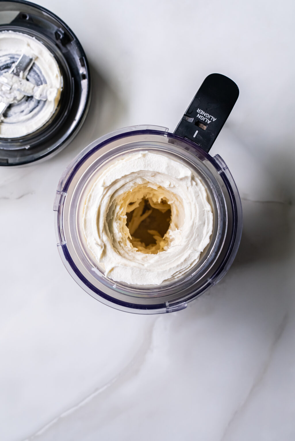 An electric Ninja Creami ice cream maker sits on a white countertop, its transparent container filled with freshly churned Coconut ice cream.