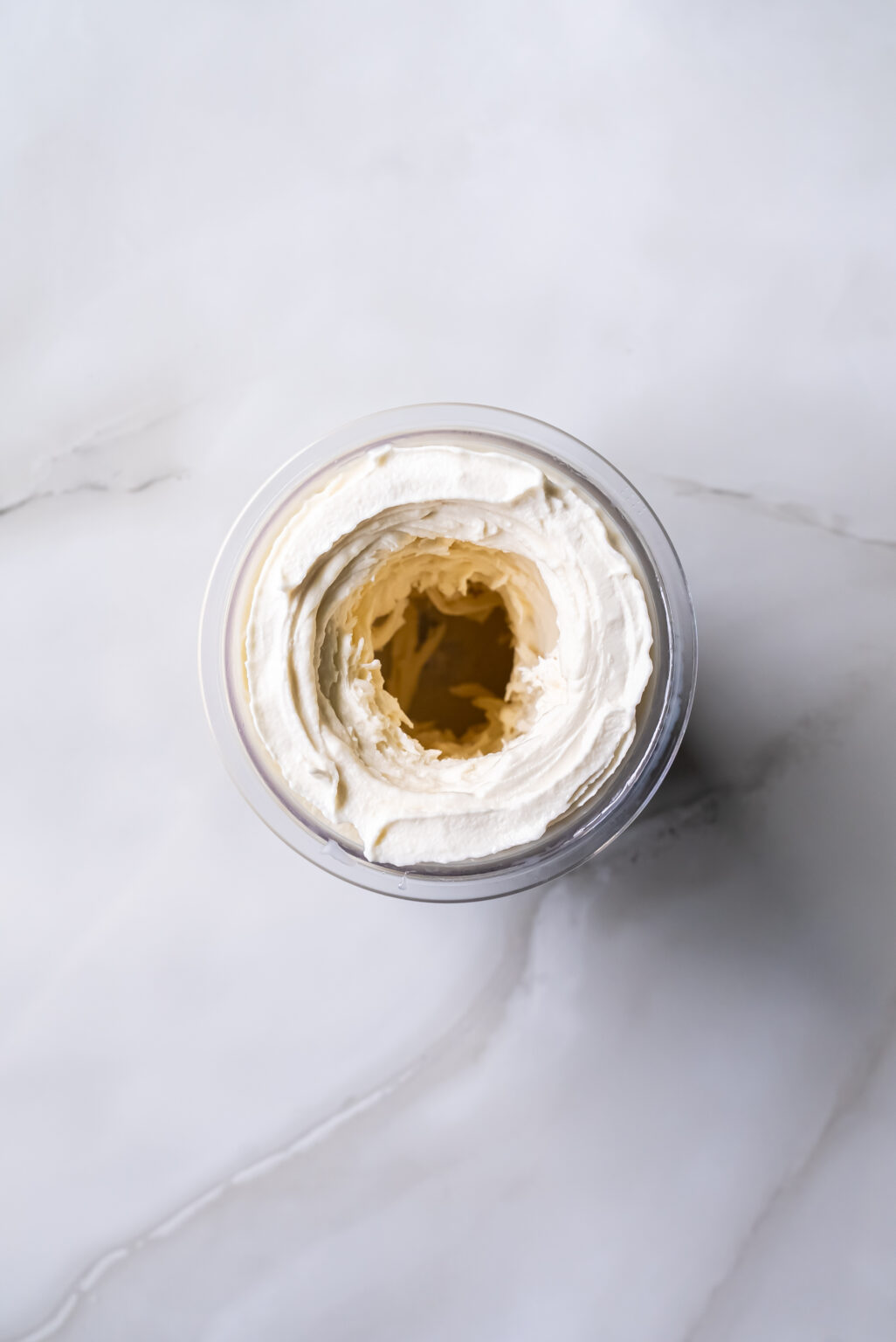 A Ninja Creami ice cream pint sits on a white countertop, its transparent container filled with freshly churned coconut ice cream.