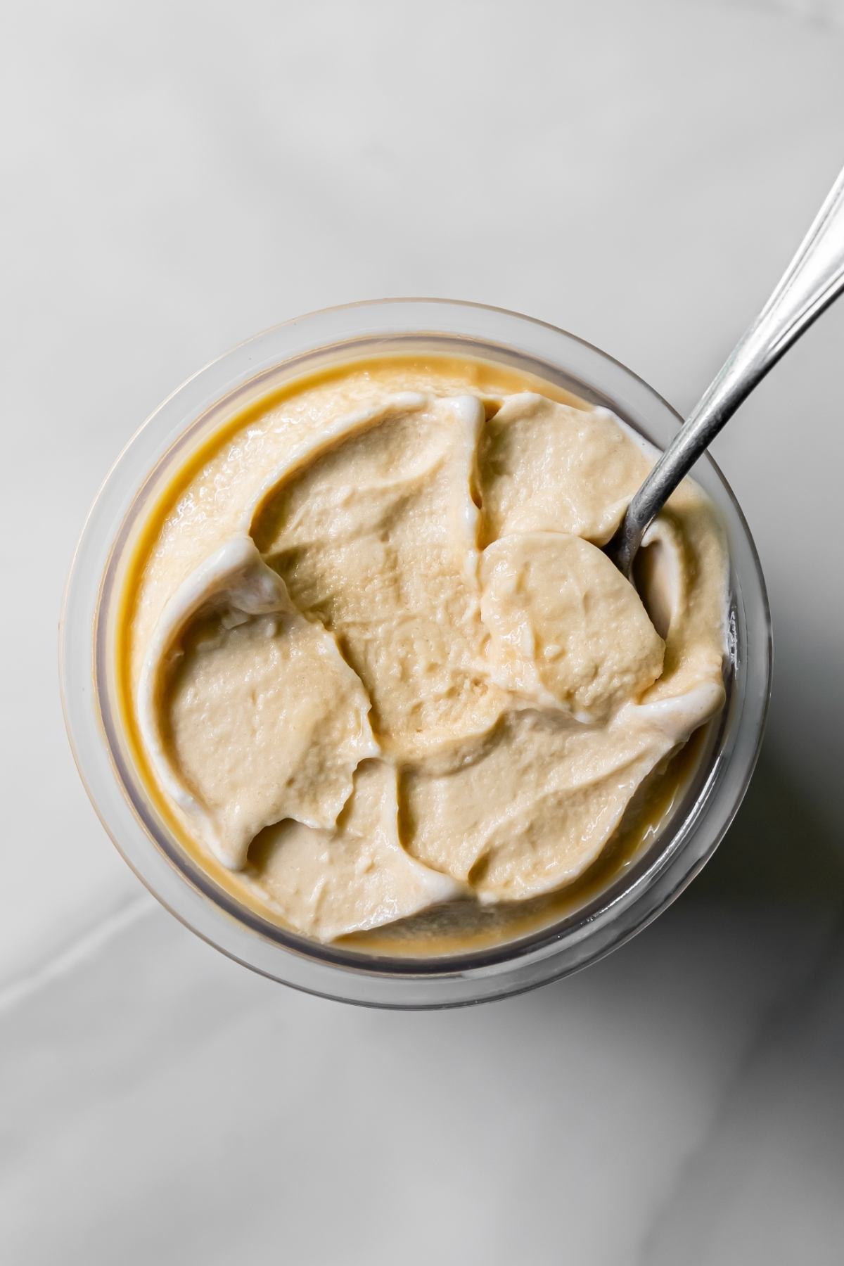 Top view of Oat Milk Protein Coffee ice cream in a clear pint with a spoon