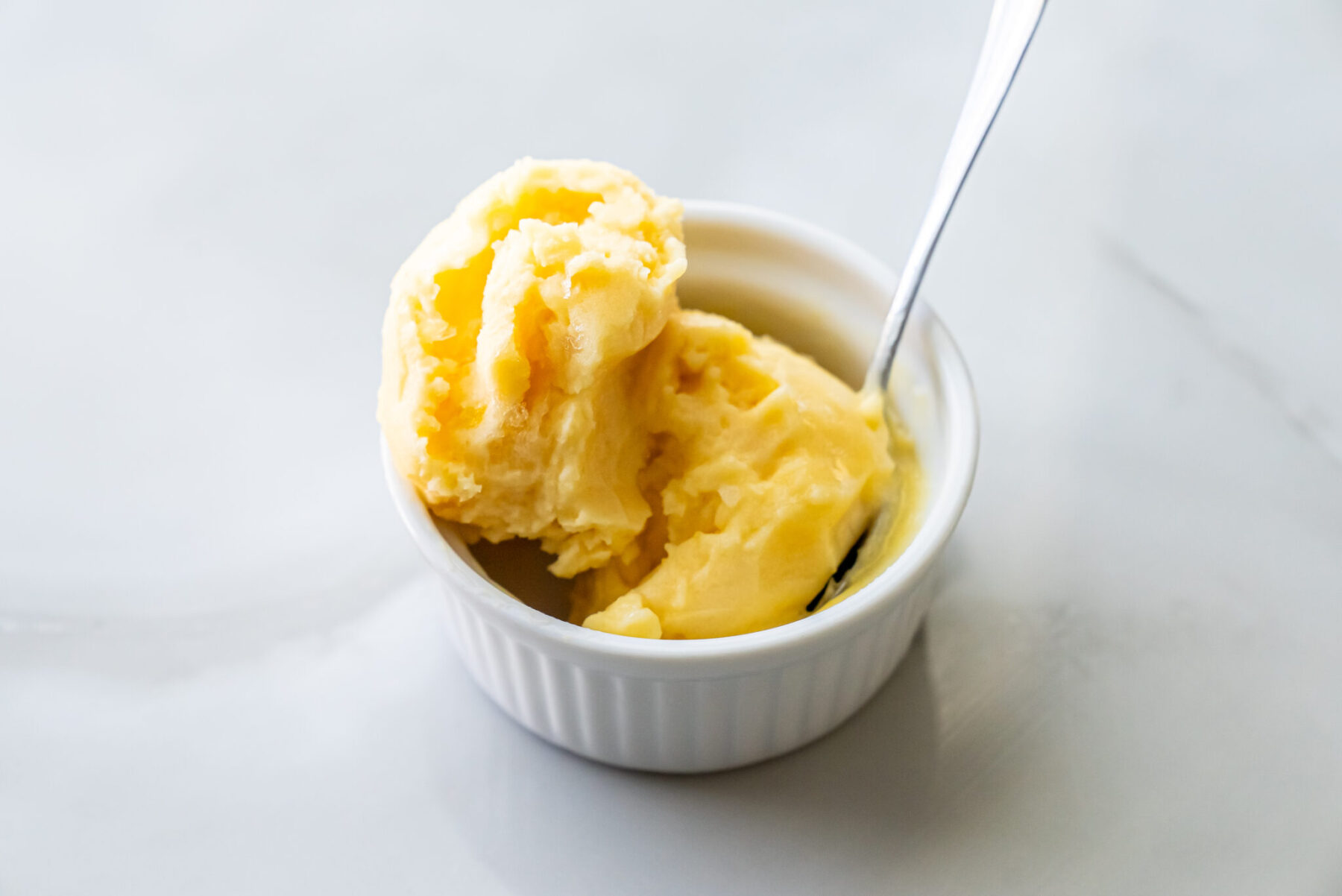 peach sorbet in a white bowl with a spoon.