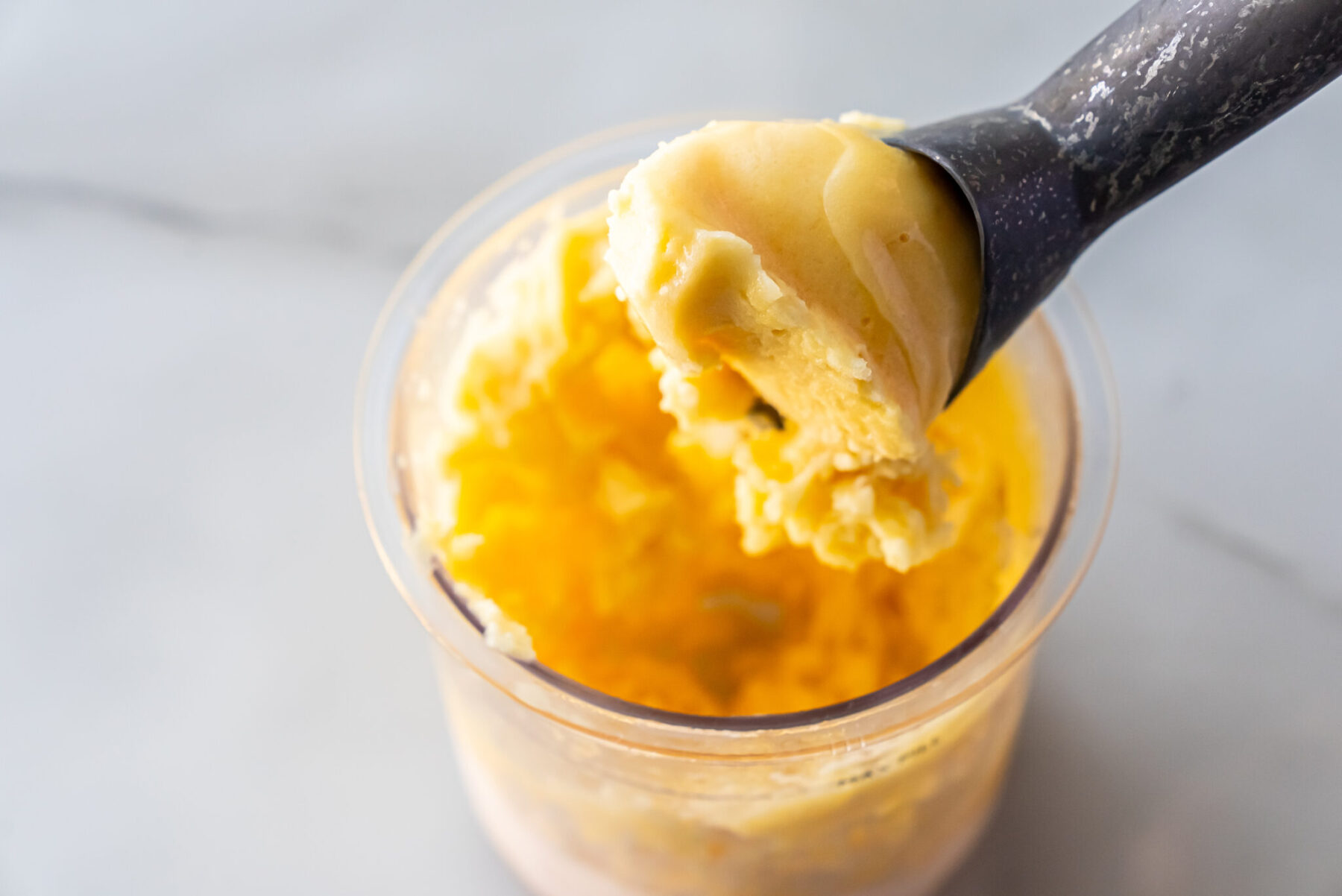 peach sorbet in a pint with an an ice cream scooper.
