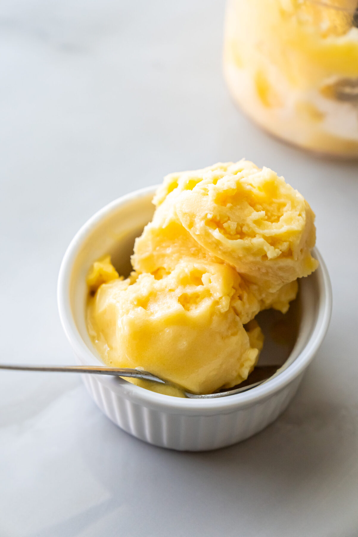 Ninja Creami peach sorbet in a white bowl with a spoon.
