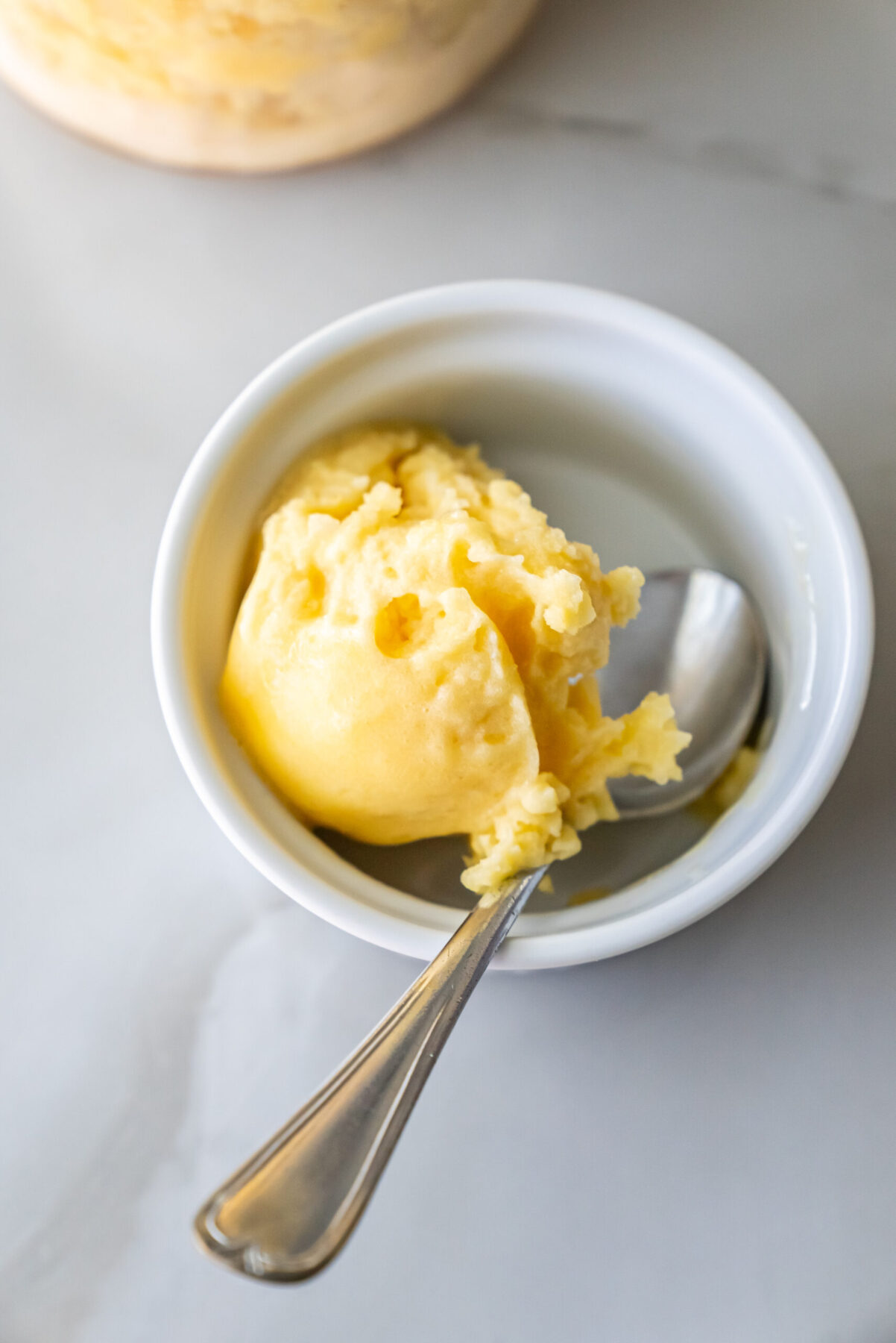 peach sorbet in a white bowl with a spoon