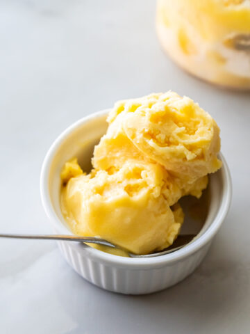 Ninja Creami peach sorbet in a white bowl with a spoon.