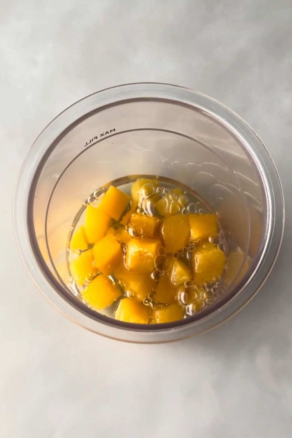 Top-down view of a clear Ninja Creami pint filled with fresh peach chunks submerged in liquid base, ready to be frozen and churned into vibrant Ninja Creami Peach Sorbet.