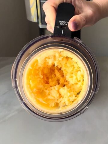 Top-down view of a Ninja Creami pint showing coarse, icy peach sorbet after initial spin — textured and uneven, awaiting re-spin or mix-in to achieve smooth Ninja Creami Peach Sorbet consistency.