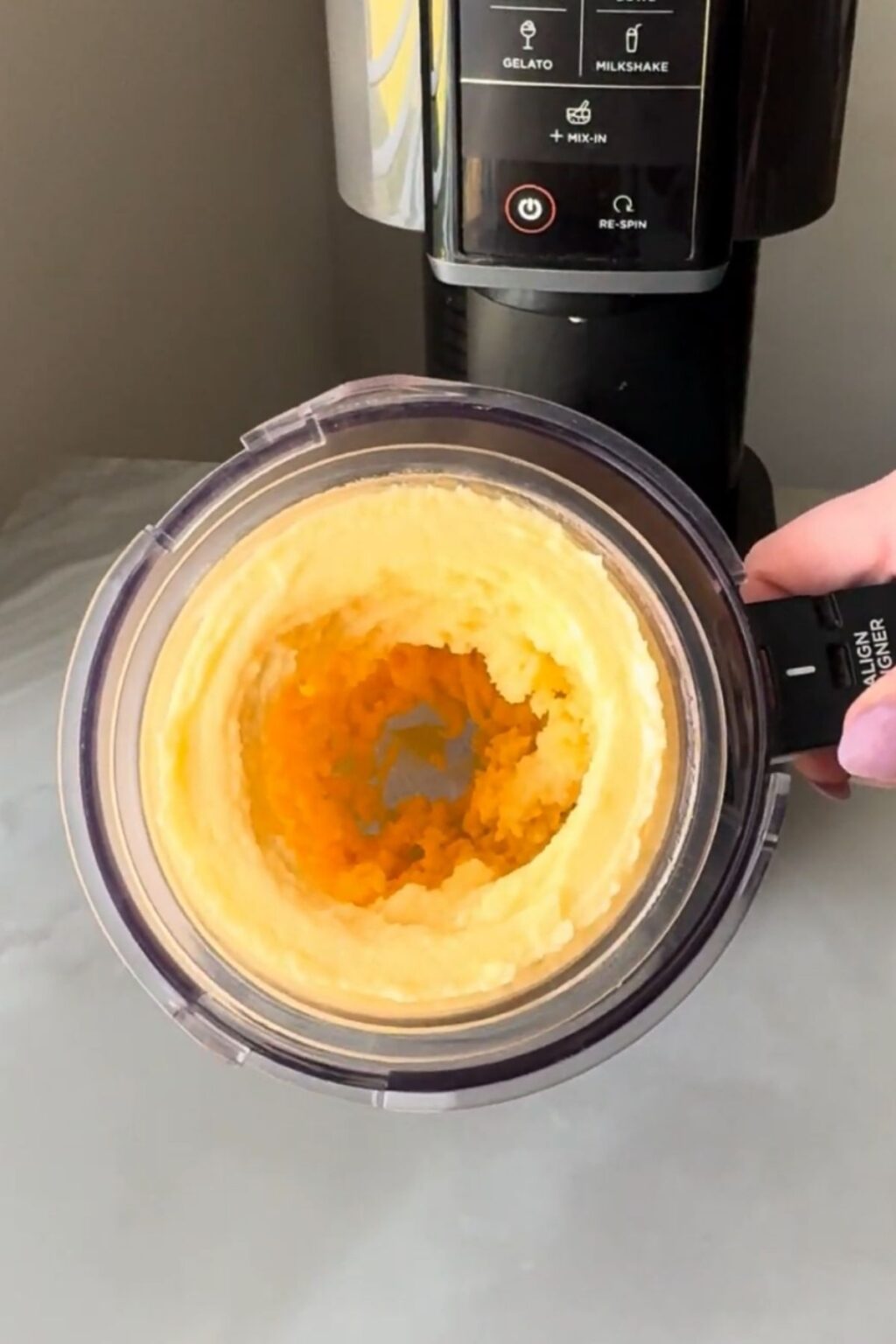 Close-up of a Ninja Creami pint displaying improved, creamier peach sorbet texture after re-spin, with visible swirls and reduced iciness, nearing final Ninja Creami Peach Sorbet perfection.
