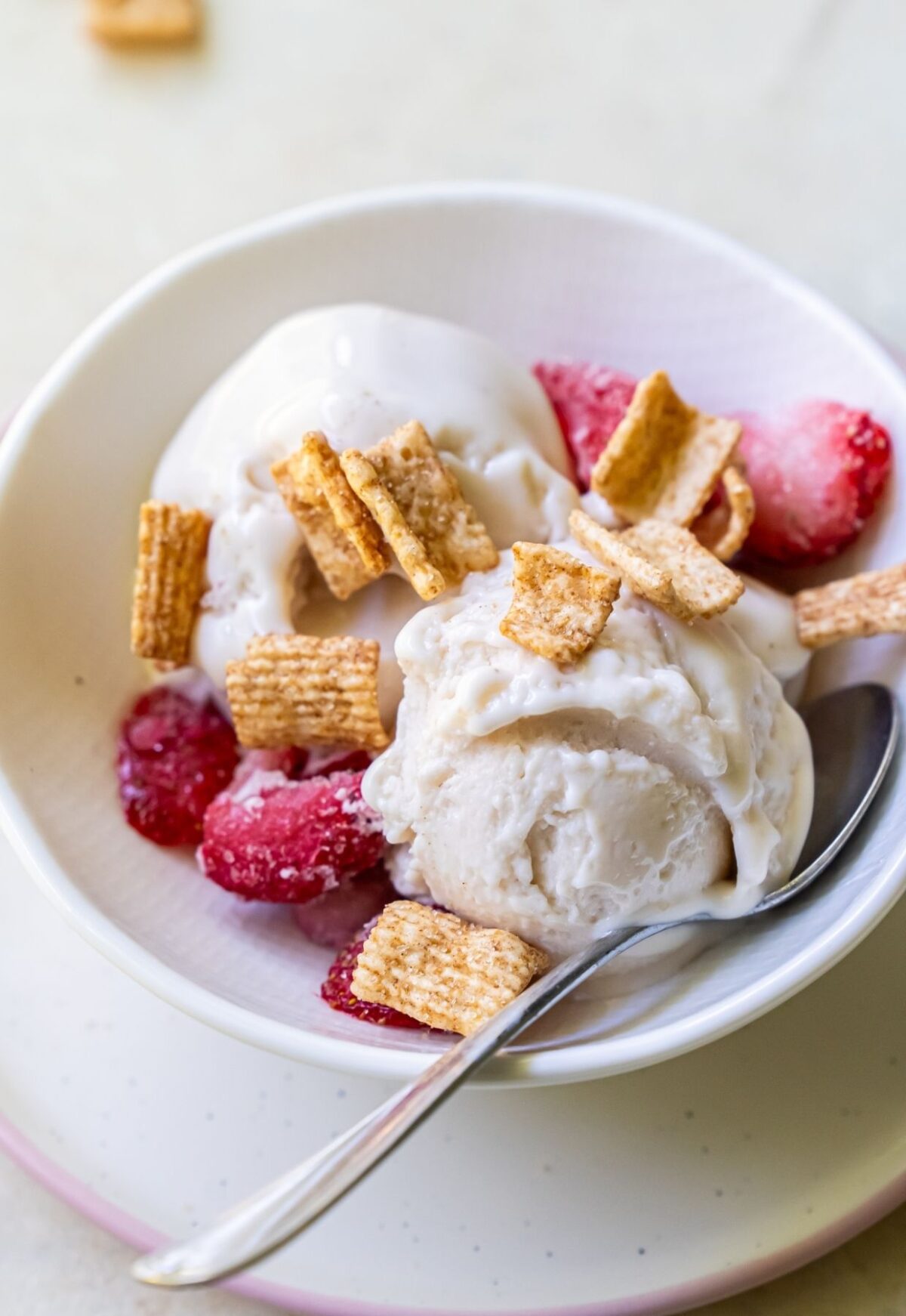 A bowl of refreshing protein ice cream topped with cereal flakes and fresh strawberries, with a spoon placed on the side.