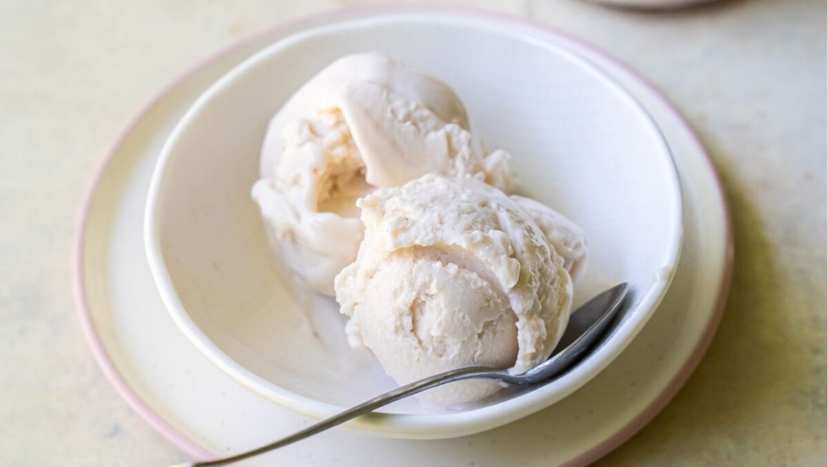 A bowl with two scoops of cheesecake ice cream and a spoon on a light-colored plate, made using the Ninja Creami for that perfect texture.