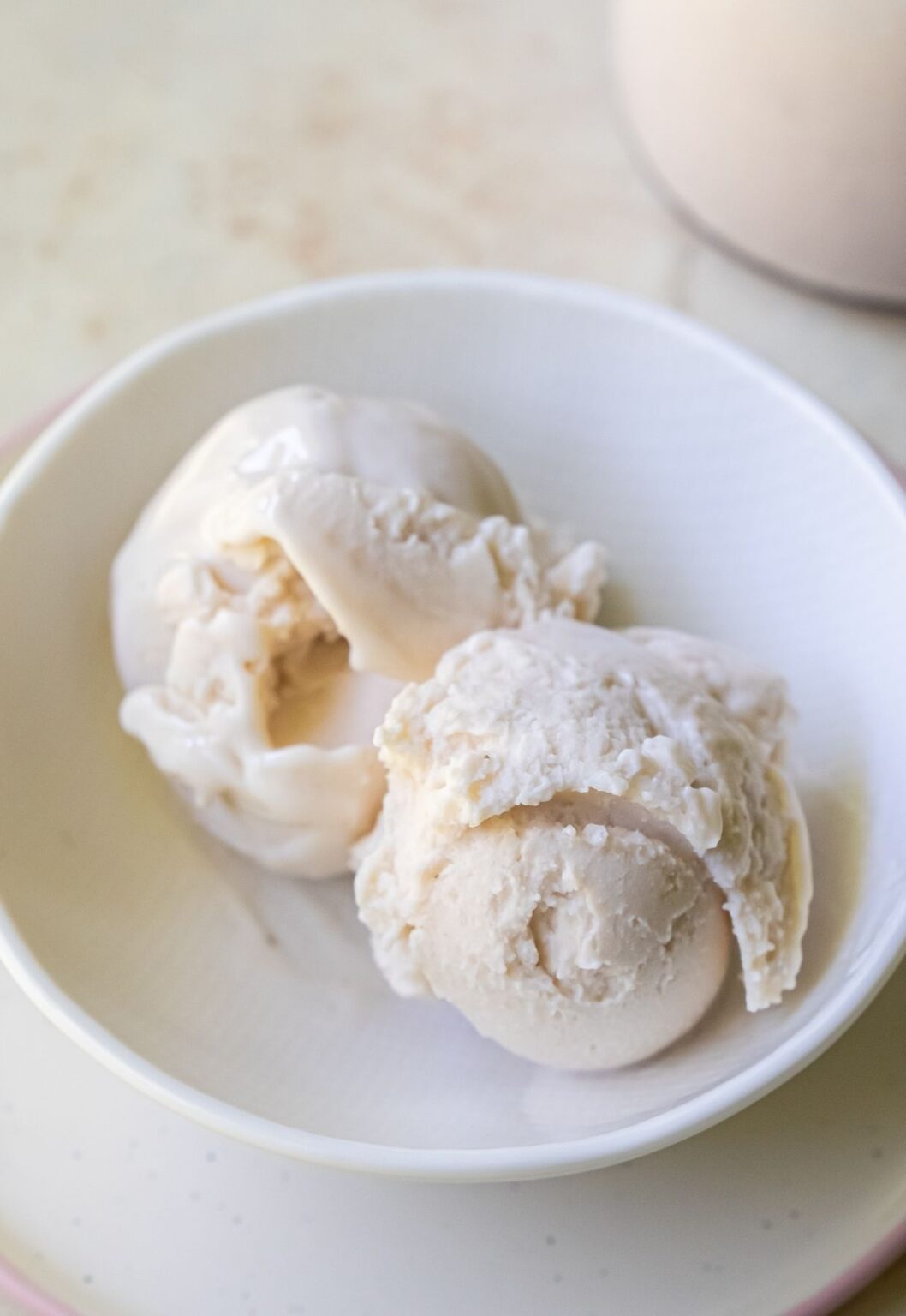 A white bowl contains two scoops of Ninja Creami vanilla ice cream on a light surface.