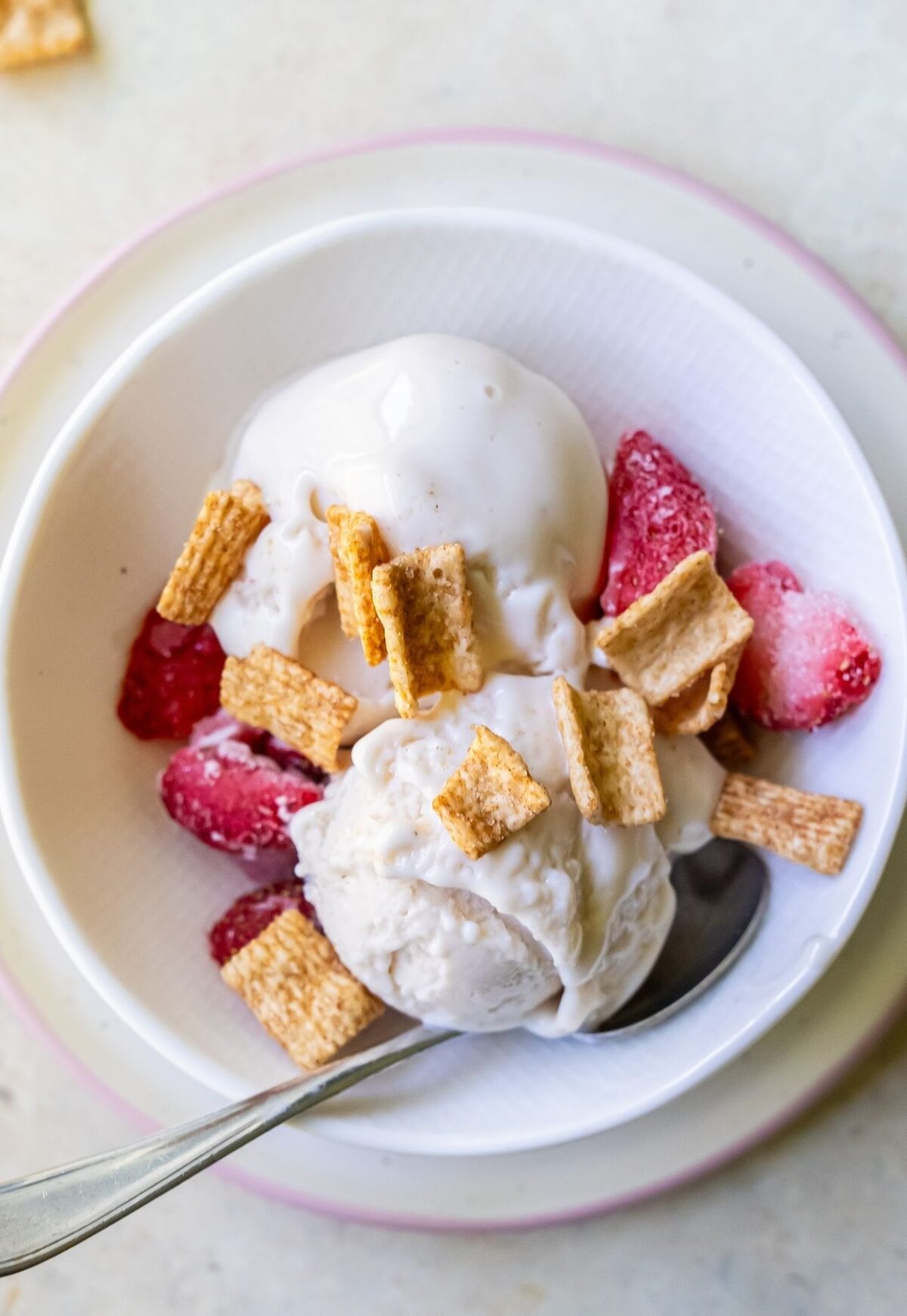 A bowl of vanilla ice cream topped with freeze-dried strawberries and cereal pieces, reminiscent of a Strawberry Cheesecake, with a spoon in the bowl.