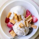 A bowl of vanilla ice cream topped with freeze-dried strawberries and cereal pieces, reminiscent of a Strawberry Cheesecake, with a spoon in the bowl.
