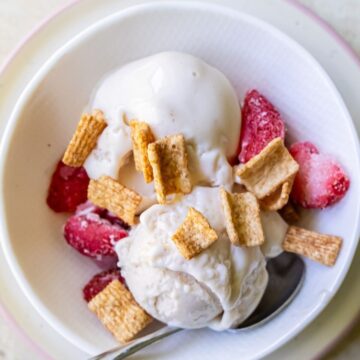 A bowl of vanilla ice cream topped with freeze-dried strawberries and cereal pieces, reminiscent of a Strawberry Cheesecake, with a spoon in the bowl.