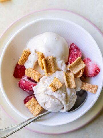A bowl of vanilla ice cream topped with freeze-dried strawberries and cereal pieces, reminiscent of a Strawberry Cheesecake, with a spoon in the bowl.